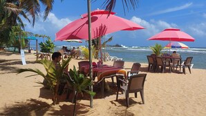 Ein Restaurant direkt am Strand mit Tischen und Stühlen unter rosa Sonnenschirmen mit Blick auf den Ozean.