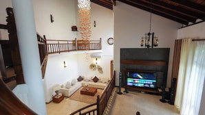 Ein geräumiges Wohnzimmer mit hoher Decke, Kamin, Fernseher und einer Treppe.