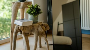 Et moderne værelse med trægulv, et stort spejl og to små træborde med plantepotteskjulere.
