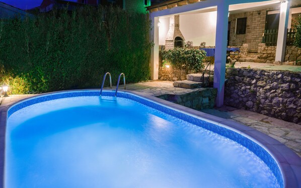 A swimming pool with a stone wall and a covered patio area.