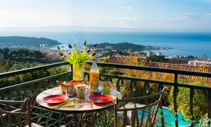 A table set with plates, cutlery, and a bottle of drink on a balcony overlooking a coastal view.