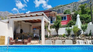 Zona de piscina amb una pèrgola, mobiliari exterior i una paret de pedra.