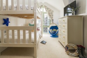 Une chambre d’enfant avec des lits superposés, un fauteuil suspendu, une commode et une fenêtre avec des rideaux.