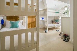 A child's bedroom with bunk beds, a small table, and a window with curtains. - Llawnroc - sleeps 10 guests  in 4 bedrooms (Bude)