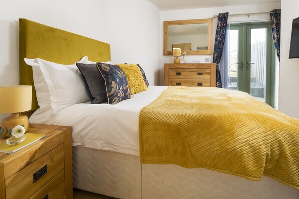 A neatly made bed with a yellow throw blanket, a bedside lamp, and a wooden nightstand with a flower vase.