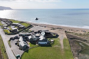 Vue aérienne d’une propriété côtière comprenant plusieurs bâtiments, une plage et un phare.