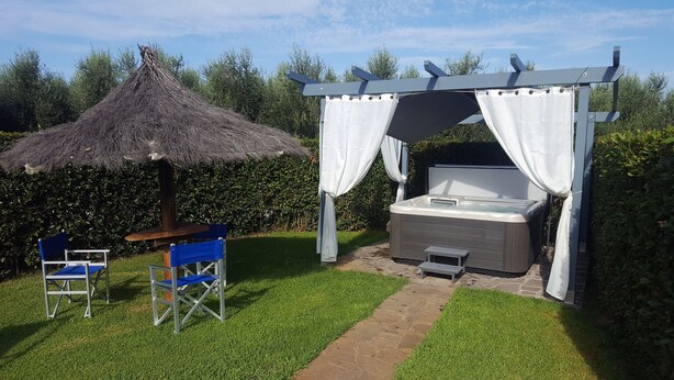 A garden with a thatched umbrella, a hot tub, and blue chairs.