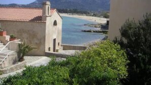 A coastal view with a building featuring a red-tiled roof and a small tower, overlooking a beach and mountains. - house / villa - Algajola (Algajola)