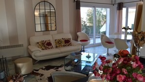 A modern living room with a white sofa, glass coffee table, and a glass dining table with chairs. There is a large mirror on the wall and a view of the outdoors through the windows. - house / villa - Algajola (Algajola)
