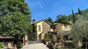 A yellow villa with a stone pathway leading to the entrance, surrounded by greenery and trees. - Villa with private pool in Tuscany (Tresana)