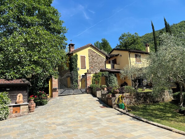 Une villa jaune avec un chemin de pierre menant à l’entrée, entourée de verdure et d’arbres.