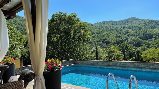 A pool with a view of a forested hill, wicker furniture, and a table. - Villa with private pool in Tuscany (Tresana)