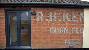 Un bâtiment en briques avec une porte en verre et une enseigne sur laquelle on peut lire : « R.H. KEN CORN FLO MEAL ».