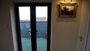 Une pièce dotée d’une porte-fenêtre coulissante qui donne sur un espace extérieur avec un sol recouvert d’herbe et un toit en tuiles. Un tableau encadré est accroché au mur, au-dessus de la porte.