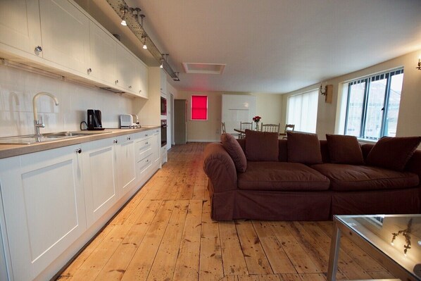 Een moderne keuken met witte kasten, een houten vloer en een bruine bank in de woonkamer.