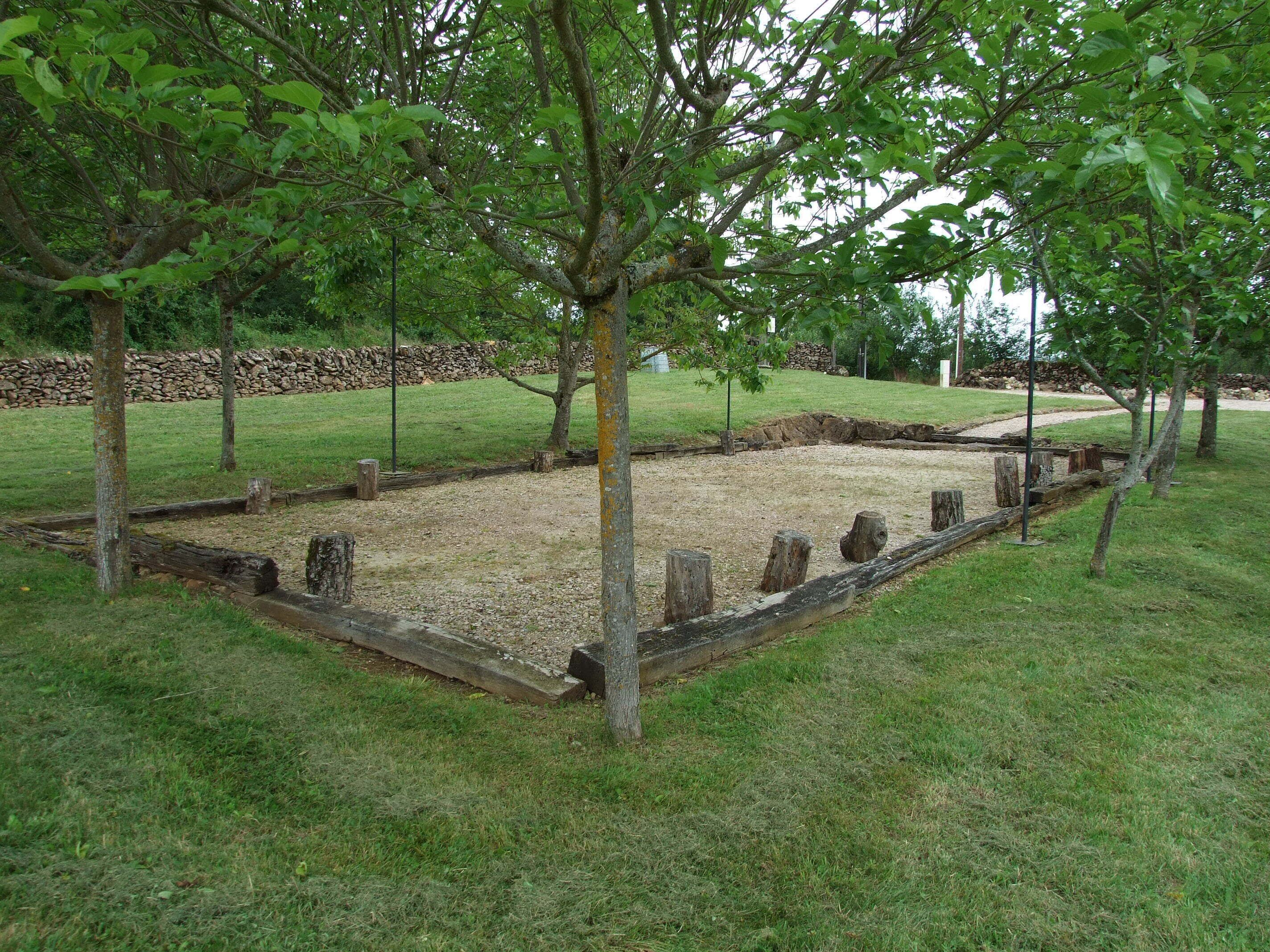 A garden with a central gravel area surrounded by trees and a stone wall in the background.