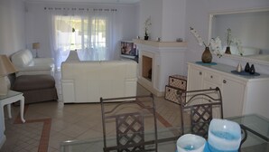 Een woonkamer met een witte bank, een glazen salontafel en een open haard.