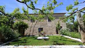A stone building with a garden in front, including a small fountain and white flowers.