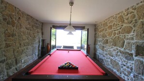 A pool table with a red felt surface, surrounded by stone walls, and a hanging light fixture above.