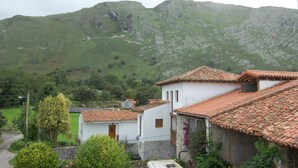 Ein ländliches Dorf mit traditionellen weißen Gebäuden und roten Ziegeldächern, umgeben von grünen Hügeln und Bergen.