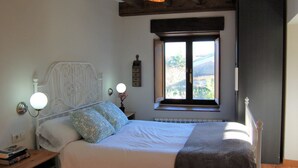 Ein Schlafzimmer mit Bett, Nachttisch, Lampe, Fenster und Blick ins Freie.