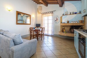Un salon comprenant un canapé, une table à manger avec des chaises, un téléviseur et un coin cuisine avec une cuisinière et des étagères.