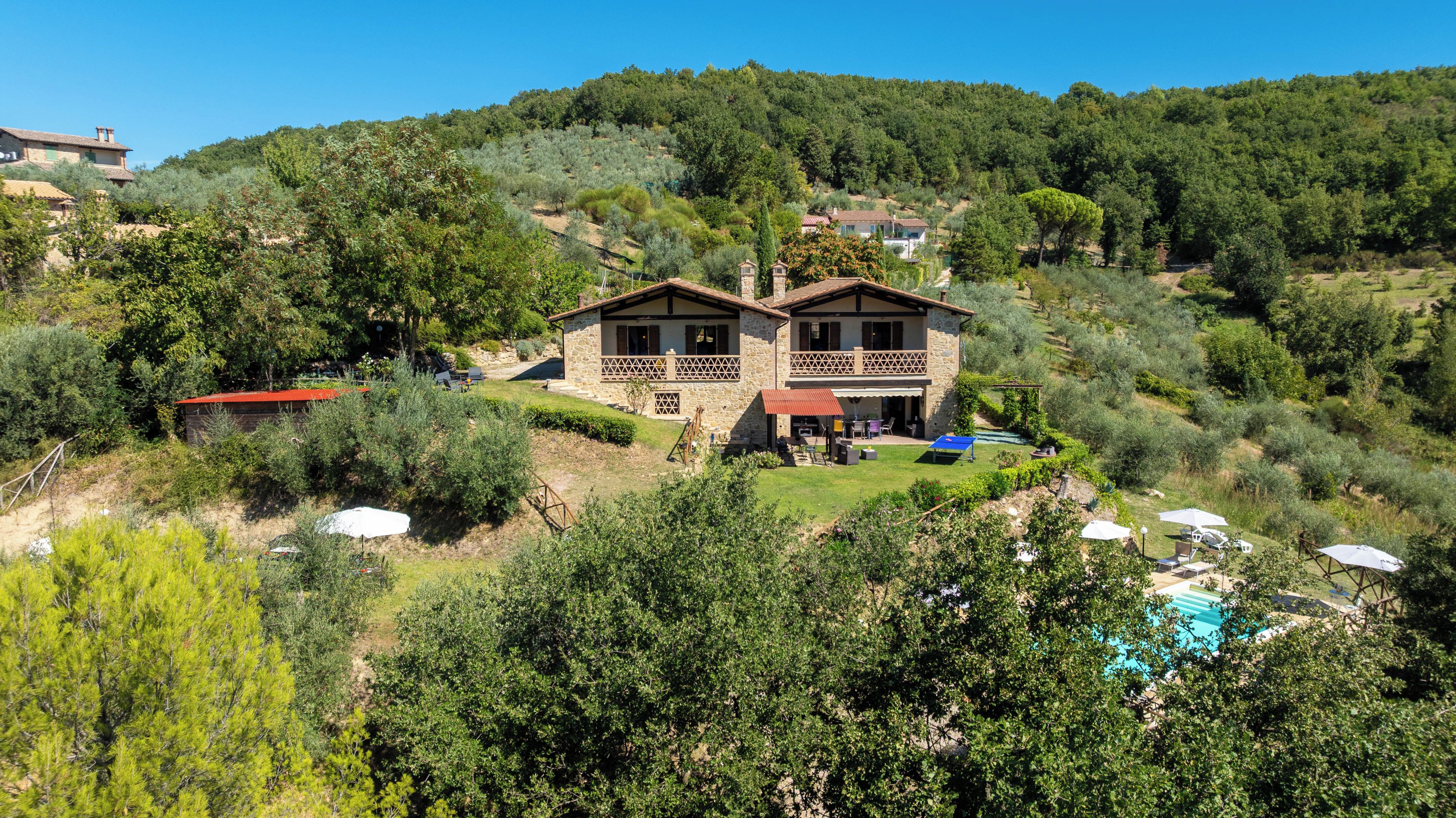 Une maison en pierre à deux étages, dotée d’un balcon, entourée de verdure et agrémentée d’une piscine.
