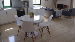 A modern kitchen with white cabinets, a microwave, and a coffee maker. There is a dining area with a white table and chairs, and a sofa in the living room. - Buenavista, 2 bedrooms, Wifi, very sunny, terrace, sea views, central location (Morro Jable)