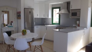A modern kitchen with white cabinetry, a stainless steel refrigerator, a built-in oven, and a dining area with a round table and white chairs. - Buenavista, 2 bedrooms, Wifi, very sunny, terrace, sea views, central location (Morro Jable)