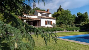 A two-story house with a swimming pool, surrounded by greenery and trees.