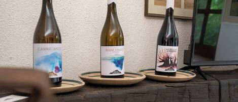 Three wine bottles on wooden coasters with labels, placed on a wooden table against a textured wall.