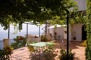 Une terrasse avec une table et des chaises, entourée de plantes en pot et offrant une vue sur la mer.