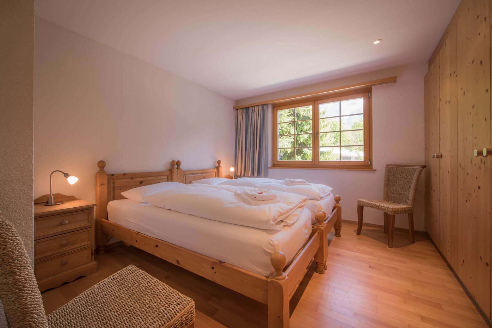Une chambre à coucher avec un lit en bois, une table de chevet avec une lampe, une chaise et une fenêtre avec des rideaux.
