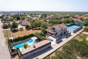 A residential area with a swimming pool, a tennis court, and houses with red roofs.
