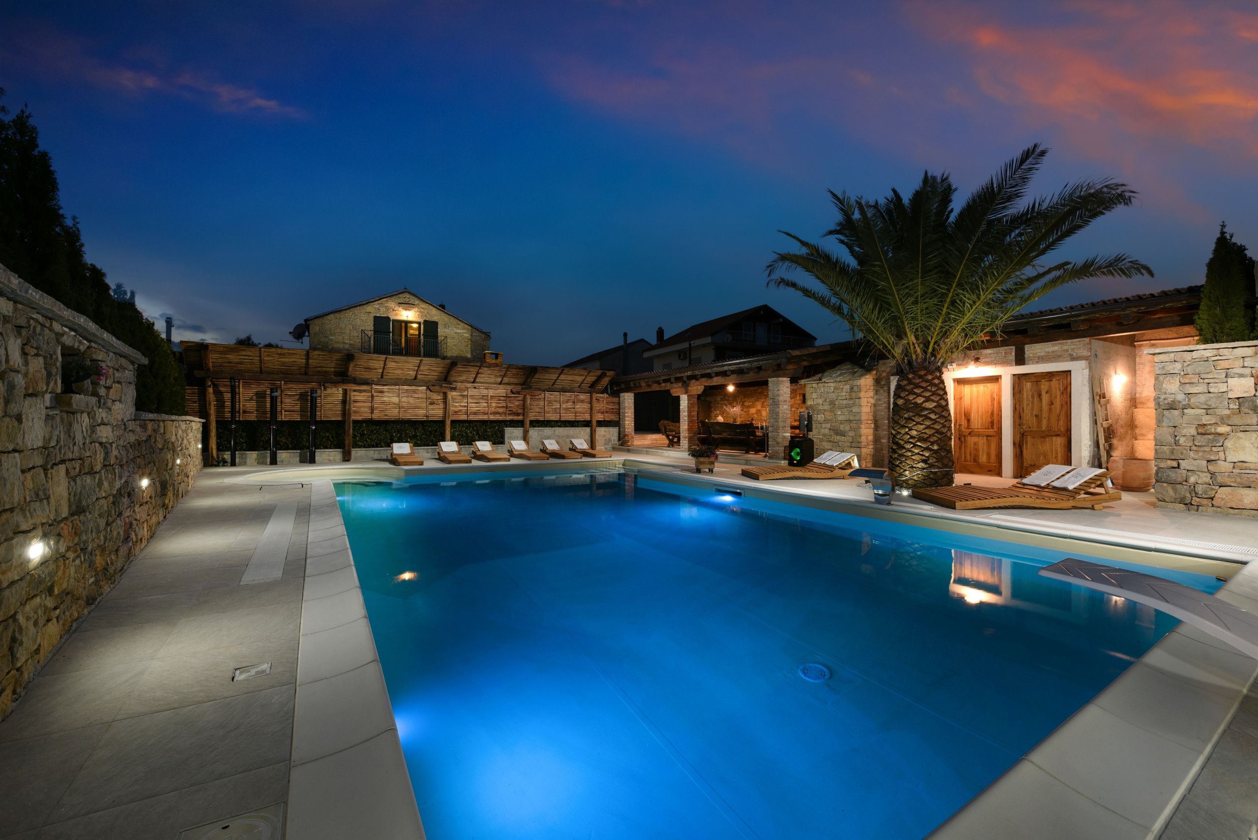 A swimming pool with lounge chairs and a stone wall.