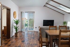 Een ruime woonkamer met een houten eettafel en stoelen, een flatscreen televisie en potplanten.