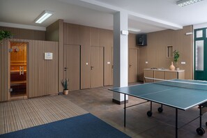 Een kamer met een tafeltennistafel, een wand van houten latten en een deur naar een sauna.