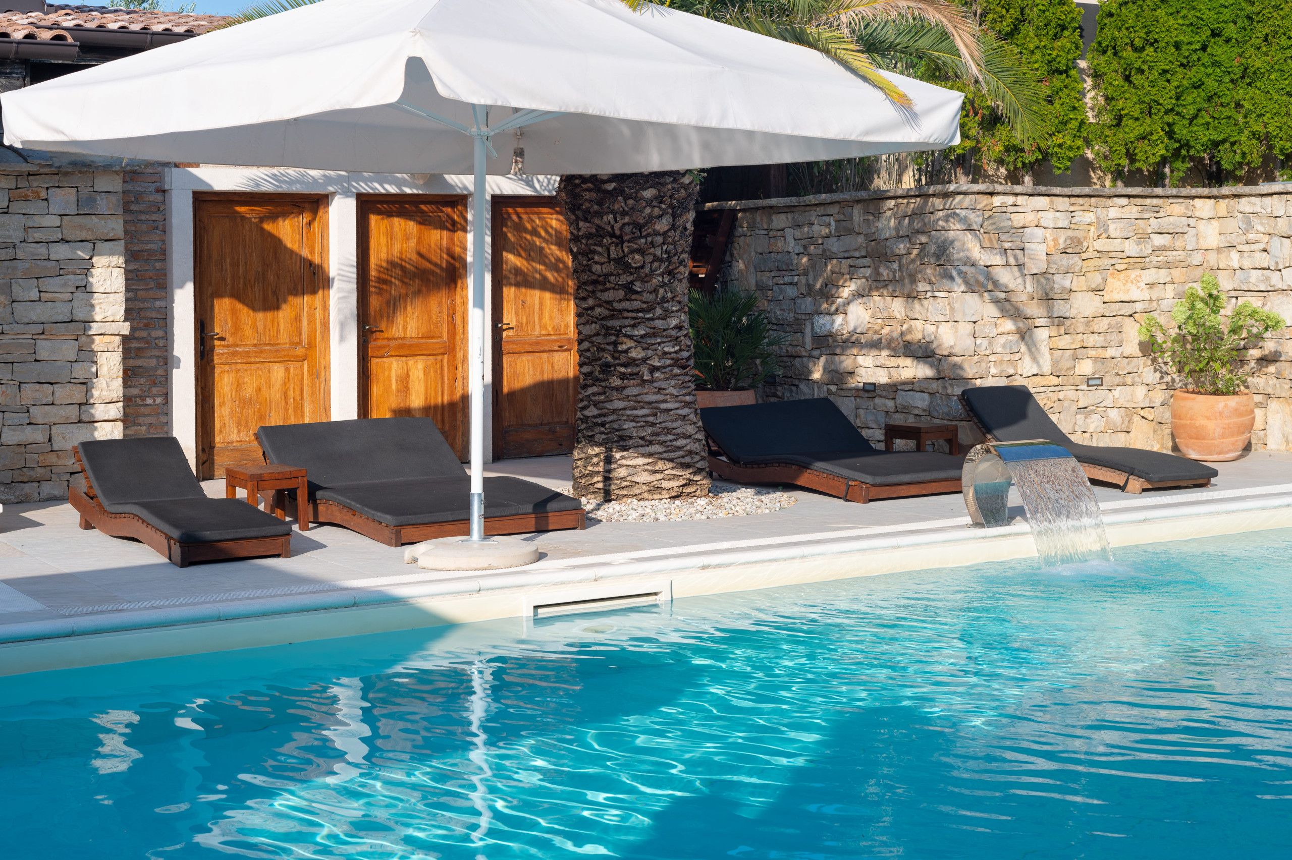 A poolside area with lounge chairs, a stone wall, and a wooden door.
