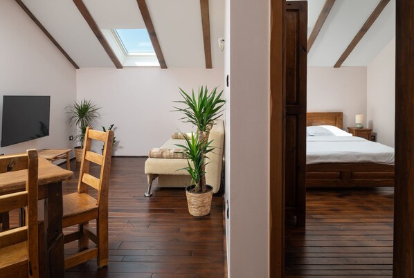 A cozy room with a wooden floor, a bed, a desk with a chair, and two potted plants.