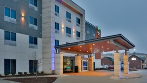 A modern hotel with a covered entrance, multiple floors, and a visible parking area. - Holiday Inn Express Suites Plano East Richardson (Celina)