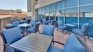 An outdoor patio area with wicker furniture and blue cushions, large windows, and a view of the cityscape. - Holiday Inn Express Suites Plano East Richardson (Celina)