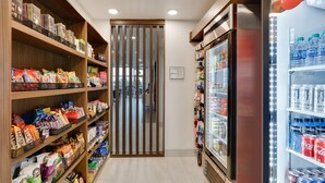 A store aisle with shelves stocked with snacks and beverages, a refrigerated display case, and a Coca-Cola refrigerator. - Holiday Inn Express Suites Plano East Richardson (Celina)