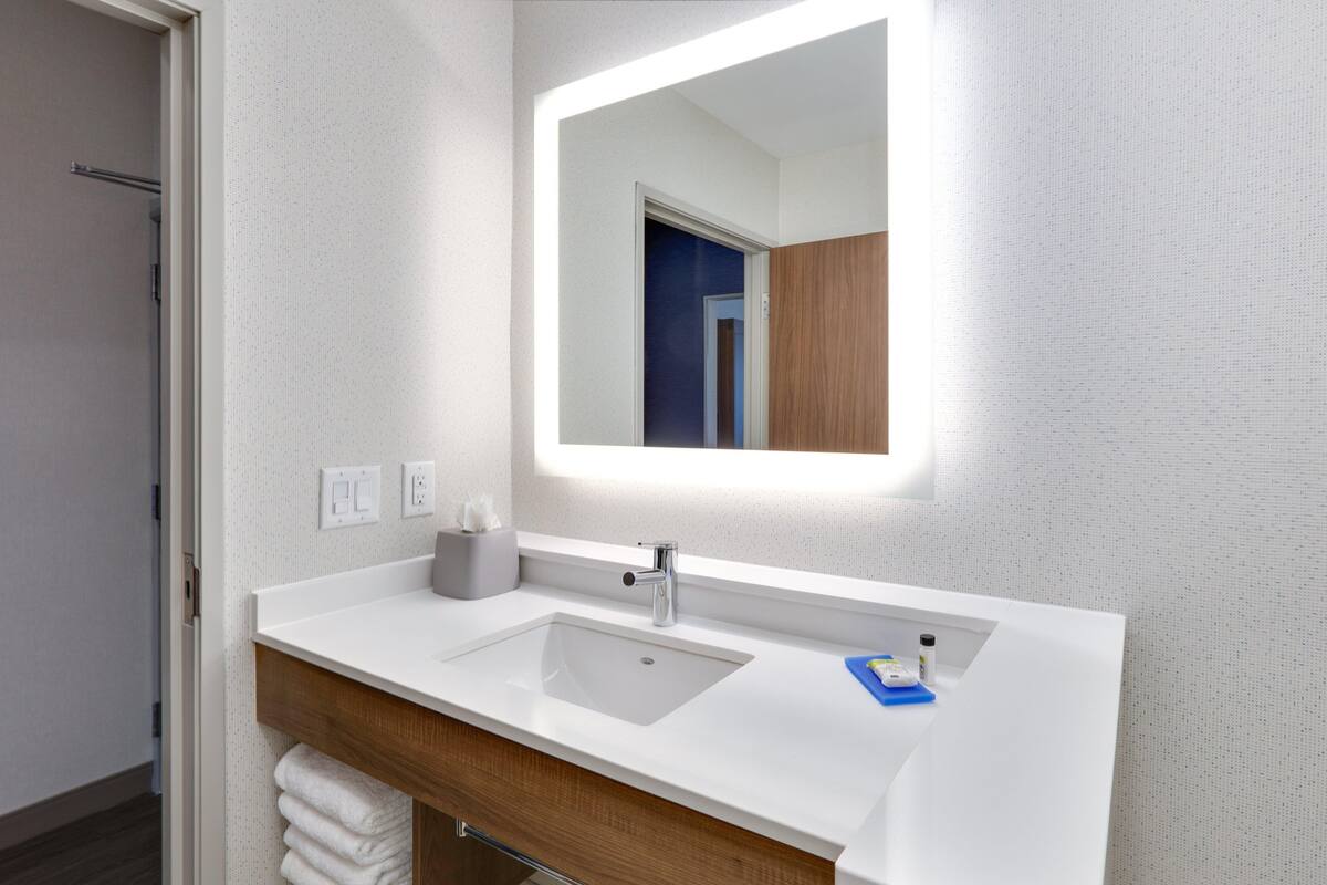 A modern bathroom with a white sink, a mirror, and a wooden vanity.