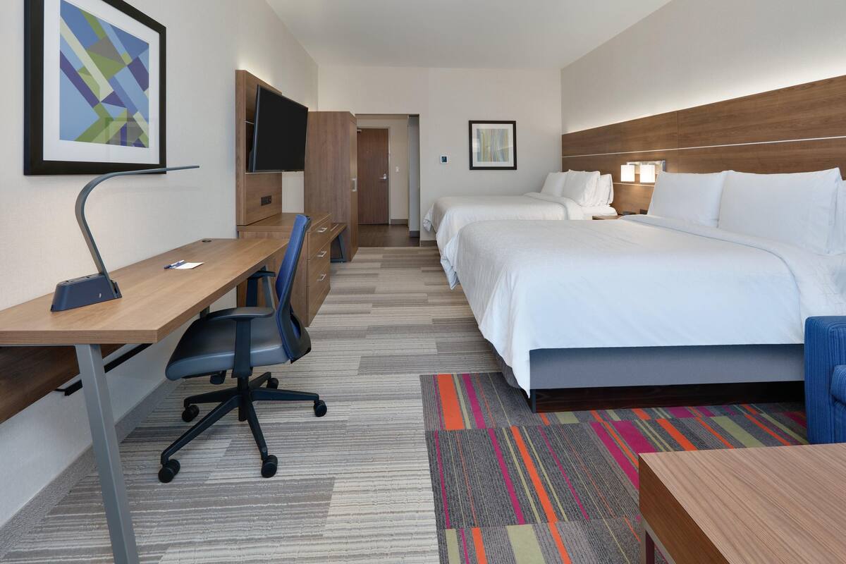 Una habitación de hotel con escritorio, dos camas, televisor y una alfombra colorida.