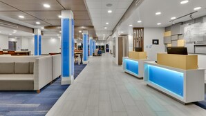 A modern hotel lobby with a central reception desk, seating areas, and a long corridor leading to other rooms. - Holiday Inn Express Suites Plano East Richardson (Celina)