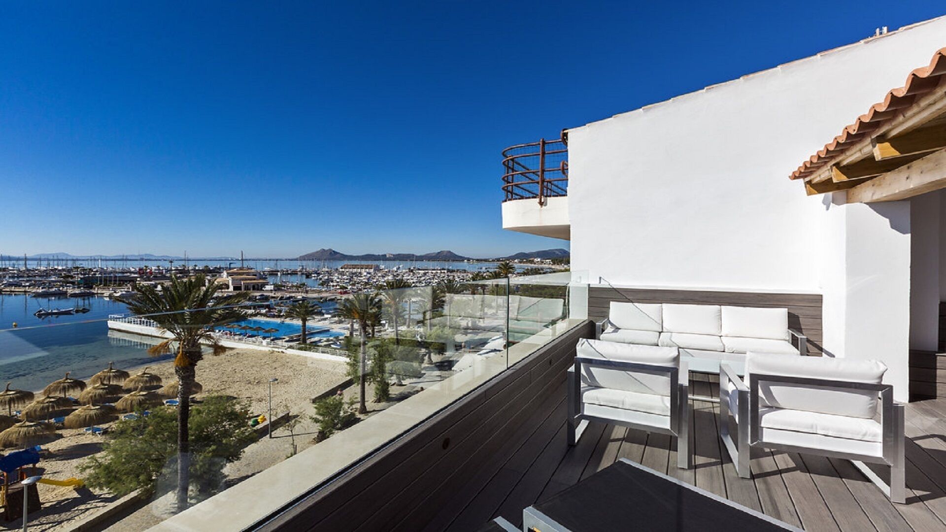 A balcony with a view of a marina, a pool, and a mountain in the distance.