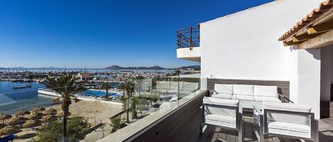 A balcony with a view of a marina, a pool, and a mountain in the distance.
