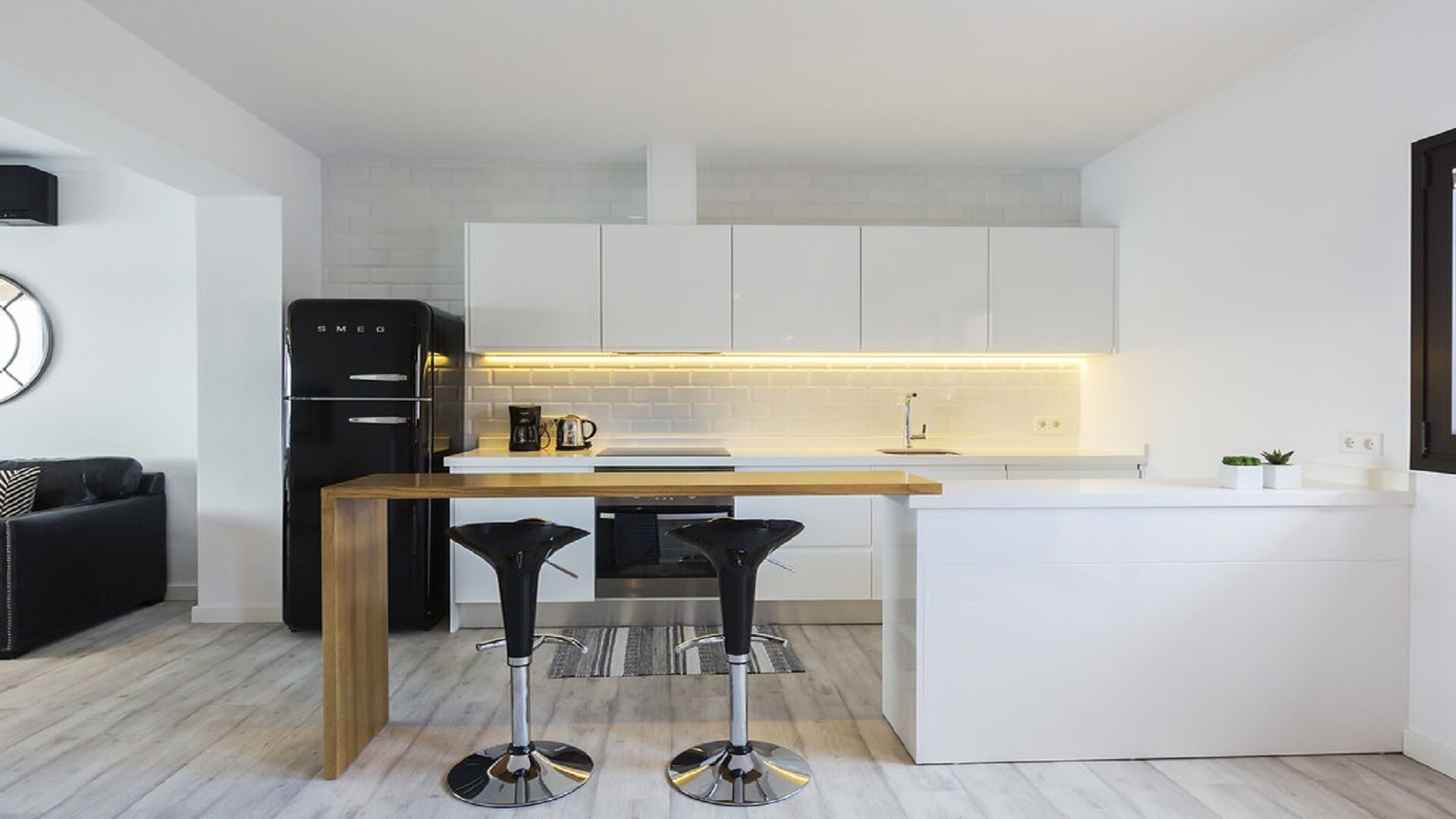 Una cocina moderna con armarios blancos, encimera de madera y dos taburetes negros.