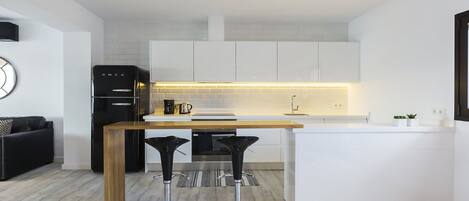 Una cocina moderna con armarios blancos, encimera de madera y dos taburetes negros.