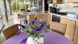A modern kitchen with a dining area, large windows, and a central island with a vase of purple flowers. - VILLA SECRET PARADISE COSTA BRAVA
Panoramic views & relax just 12m from beaches (Lloret de Mar)